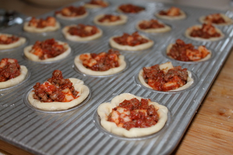 Mini muffin tins filled with stuffed pizza pie bites ready for the oven.