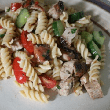 A serving of turkey & pesto pasta salad on a cream colored dinner plate.