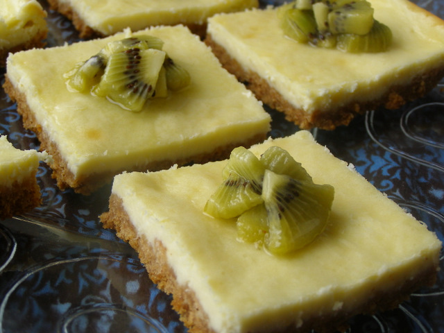 Slice of Kiwi-Glazed Cheesecake Bars on a glass serving platter.