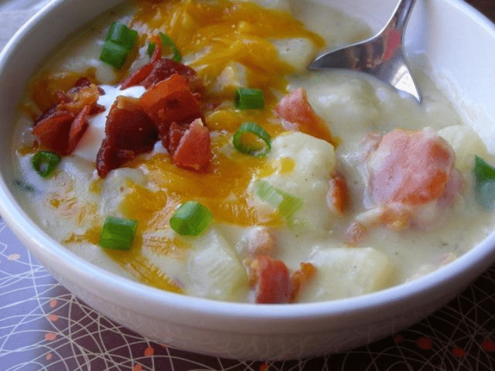 A serving of loaded baked potato soup garnished with cheese, bacon and green onion