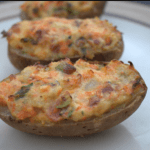 Three loaded baked potatoes with veggies lined up on a dinner plate.