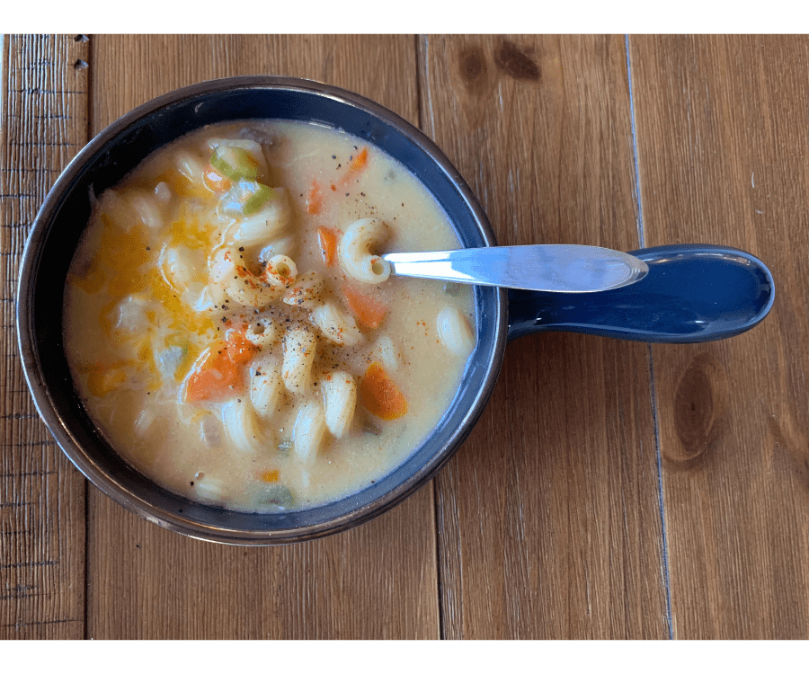 A serving of mac and cheese soup in a blue-handled bowl.
