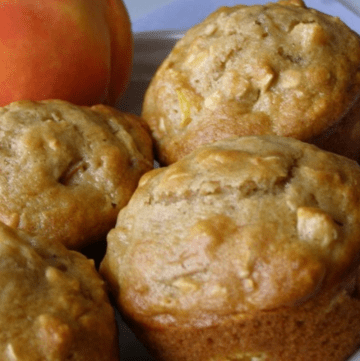 four peach muffins on a plate with a fresh peach