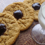 3 peanut butter jelly thumbprint cookies on a plate with a small glass of milk.